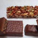 Mehrere Proteinriegel mit Schokoladenüberzug, teils aufgeschnitten, und ein Nussriegel