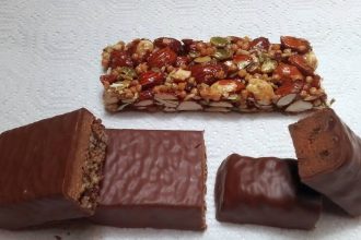 Mehrere Proteinriegel mit Schokoladenüberzug, teils aufgeschnitten, und ein Nussriegel