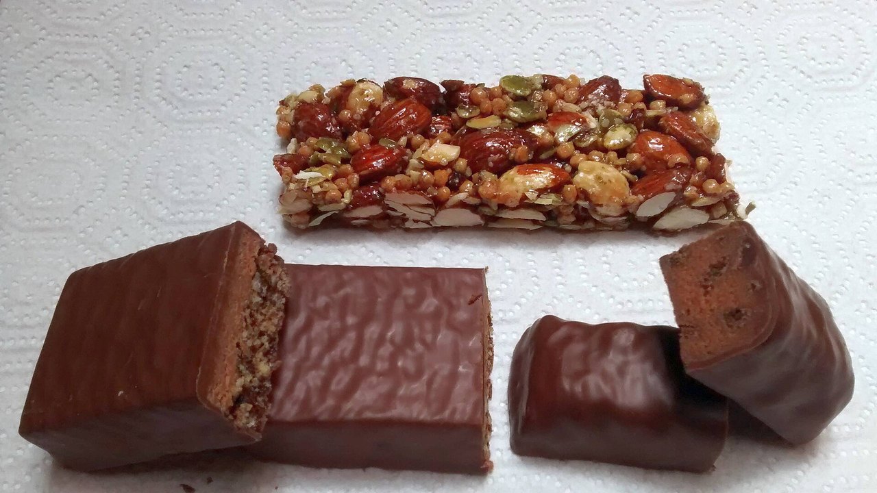 Mehrere Proteinriegel mit Schokoladenüberzug, teils aufgeschnitten, und ein Nussriegel