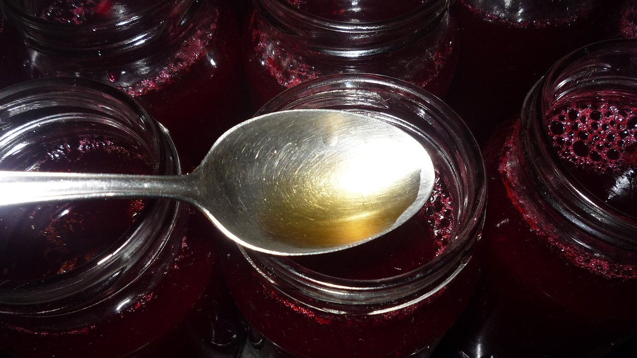 Gläser mit dunkelrotem Johannisbeer-Fruchtaufstrich, ein Löffel liegt darüber