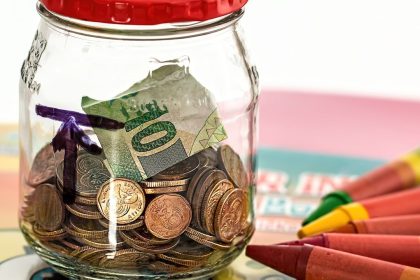 Spardose aus Glas mit Münzen und Buntstiften als Symbol für die Frühstart-Rente
