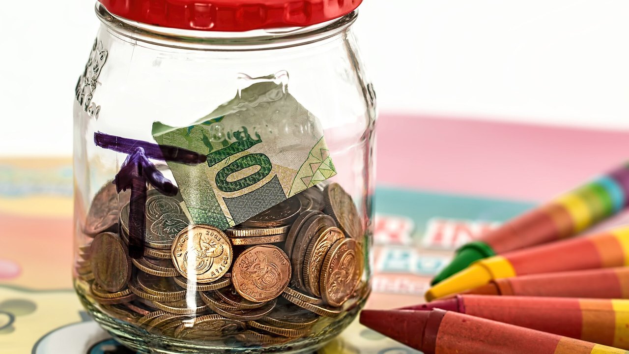 Spardose aus Glas mit Münzen und Buntstiften als Symbol für die Frühstart-Rente